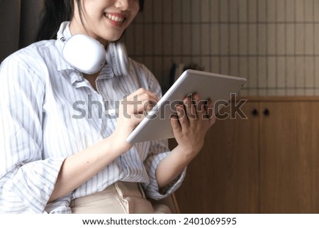 Smiling young Asian business woman leader holding digital tablet standing in office.