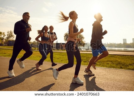 Group of sporty smiling people in sportswear jogging together in the park at sunset. Friends running outdoor having sport training in nature. Team of runners on workout. Sport and fitness concept. Royalty-Free Stock Photo #2401070663