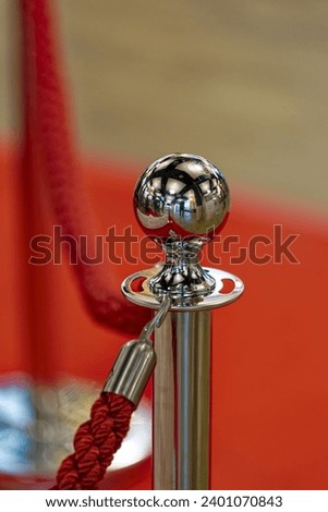 Close-up of barrier with metal pole with globe on top with red rope and red carpet in the background inside of department store. Photo taken December 13th, 2023, Zurich, Switzerland.