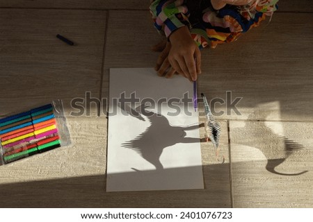 child traces contrasting shadows of toy dinosaur with felt-tip pen. drawing by primary school student, creative ideas for creativity. Interesting activities for children. play of light and shadow