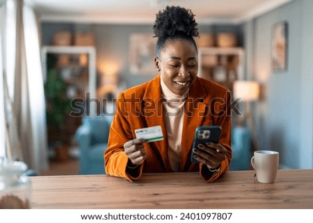 Happy young woman customer shopper holding credit card using cell phone mobile app paying online making purchase in e-commerce digital store on smartphone at home.