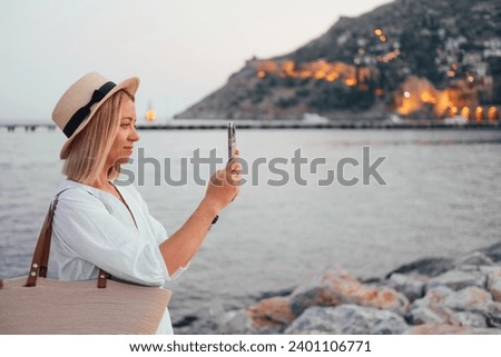 Young woman in a straw hat taking a picture of a Mountain View, with sea, castle and evening lights 