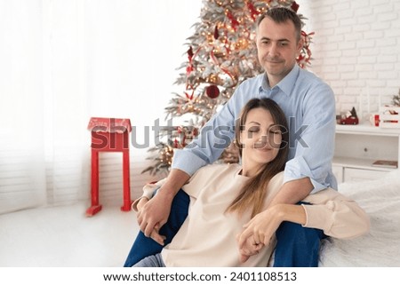 a man and a woman hugged and are sitting on a bed in a large, beautiful room decorated for Christmas. family near the New Year tree in a bright, white room.