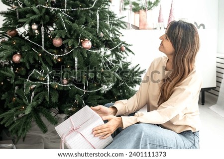 a beautiful girl with long dark hair sits near a decorated New Year tree with a gift in her hands. waiting for christmas.