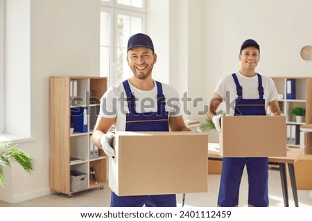 Moving company workers in uniforms take parcels from a modern office. Two happy, cheerful, smiling men from the delivery service carry cardboard boxes to load in their van Royalty-Free Stock Photo #2401112459