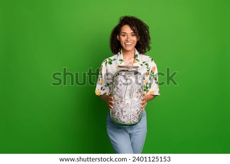 Photo of excited funky lady wear print shirt holding money jar empty space isolated green color background