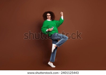 Full size profile portrait of delighted positive girl hold smart phone raise fist accomplishment isolated on brown color background