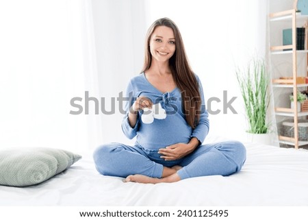 Photo of lovely cute mama attractive cheerful pregnant girl holding tiny small white socks sitting in light room indoors