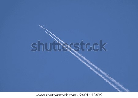 Large two engine passenger supersonic aircraft flying from right to left high in blue cloudless sky leaving two long white trails Royalty-Free Stock Photo #2401135409
