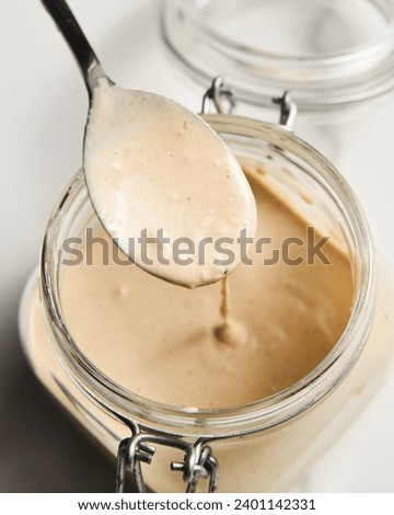 Tarator - Lebanese sauce from tahini with garlic, lemon juice and water. White or cream colored sauce in a jar on a marble background Royalty-Free Stock Photo #2401142331