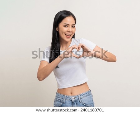 Pretty Young beautiful Asian woman standing and smiling showing mini heart sign on isolated white background. Attractive Lovely Latin female wearing white shirt feeling surprised and happy.