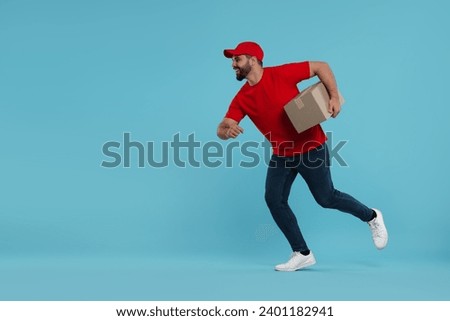Happy young courier running to deliver parcel on light blue background, space for text Royalty-Free Stock Photo #2401182941