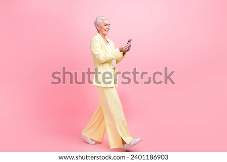 Full size photo of intelligent woman dressed yellow suit go to empty space with smartphone in hands isolated on pink color background