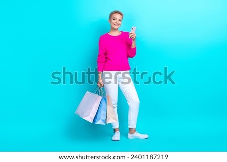 Full size photo of minded woman dressed sweater hold shopping bags smartphone look at offer empty space isolated on teal color background