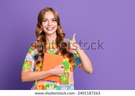 Photo of smart pretty student with wavy hair wear stylish t-shirt hold book showing thumb up recommend isolated on purple color background