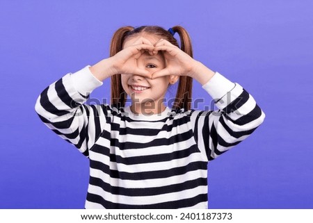 Photo of excited cute little child dressed striped pullover showing arms heart cover eye isolated purple color background