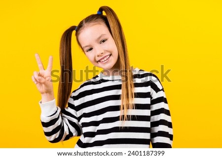 Photo of funny cheerful little child dressed striped pullover showing v-sign isolated yellow color background