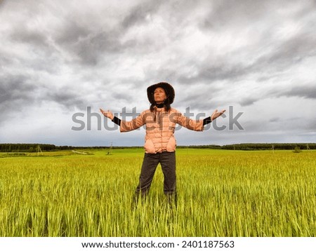 An adult girl looking like a cowboy in a hat in a field and with a stormy sky with clouds takes pictures of a rainbow and takes selfie in the rain. Woman having fun outdoors on rural and rustic nature