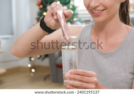 Young caucasian woman preparing healthy supplement after exercise dissolving collagen powder in glass of water..