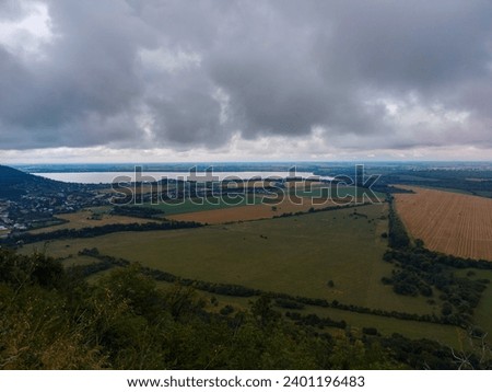 Wide horizon view of lake and fields from distance with rainy clouds and darker sky 