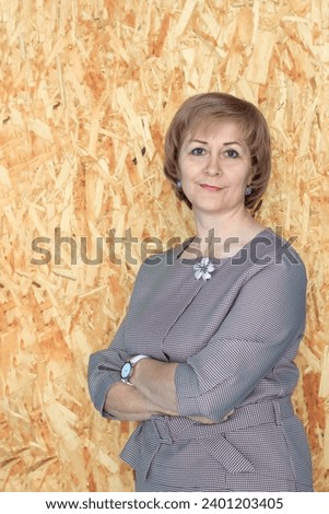 A woman stands with her hands folded against a wall with an abstract print, a business lady in a gray suit, short haircut on blond hair, calm, confident, laconic studio portrait, a self-made woman Royalty-Free Stock Photo #2401203405