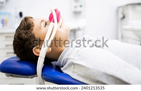 Fear of the dentist! A little boy sits in a dentist's office wearing a nasal mask breathing nitrous oxide to relax.Concept of feeling relaxed with laughing gas.Anxiety about visiting a dentist. Royalty-Free Stock Photo #2401213535