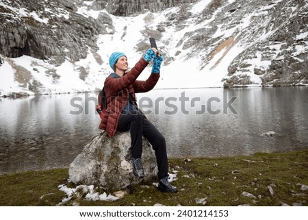 Smiling Woman Hiker Taking a Selfie Sitting on a Rock of High Mountain Alpine Lake