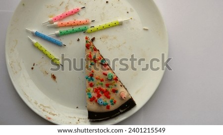 top view of a large white plate with one stale piece of cake and colored candles with a burnt wick, conceptual picture of a sad mood after party