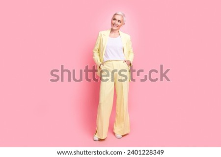 Full body photo of good mood senior person dressed yellow jacket trousers look at offer empty space isolated on pink color background