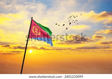 Waving flag of Eritrea against the background of a sunset or sunrise. Eritrea flag for Independence Day. The symbol of the state on wavy fabric.