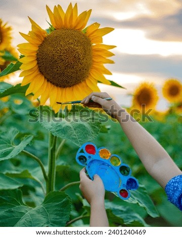A young artist paints a picturesque picture at sunset in nature in a field of sunflowers. Hands hold a palette and a brush.