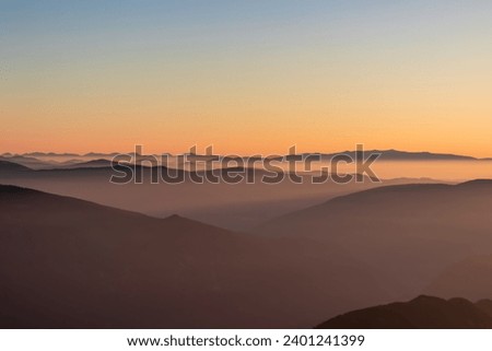 Panoramic sunrise view from Dobratsch on High Tauern and Nocky Alps in Austria, Europe. Silhouette of endless mountain ranges covered by mystical fog in valley. Jagged sharp peaks and alpine landscape Royalty-Free Stock Photo #2401241399