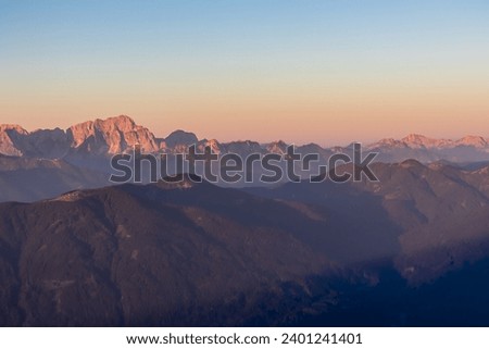 Panoramic sunrise view from summit Dobratsch on Julian Alps and Karawanks in Austria, Europe. Silhouette of endless mountain ranges with orange and pink colors of sky. Jagged sharp peaks and valleys Royalty-Free Stock Photo #2401241401