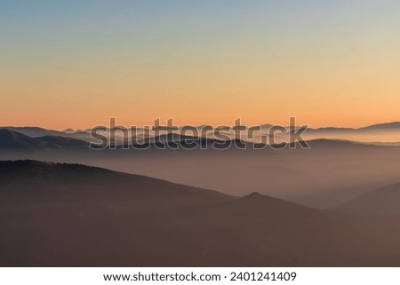 Panoramic sunrise view from Dobratsch on High Tauern and Nocky Alps in Austria, Europe. Silhouette of endless mountain ranges covered by mystical fog in valley. Jagged sharp peaks and alpine landscape Royalty-Free Stock Photo #2401241409