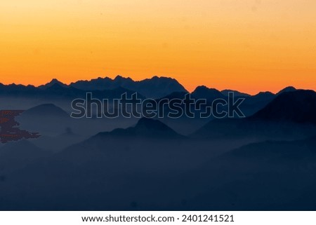 Panoramic sunrise view from Dobratsch on the Julian Alps and Karawanks in Austria, Europe. Silhouette of endless mountain ranges with orange and pink colors of sky. Jagged sharp peaks and valleys Royalty-Free Stock Photo #2401241521