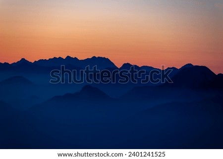 Panoramic sunrise view from Dobratsch on the Julian Alps and Karawanks in Austria, Europe. Silhouette of endless mountain ranges with orange and pink colors of sky. Jagged sharp peaks and valleys Royalty-Free Stock Photo #2401241525