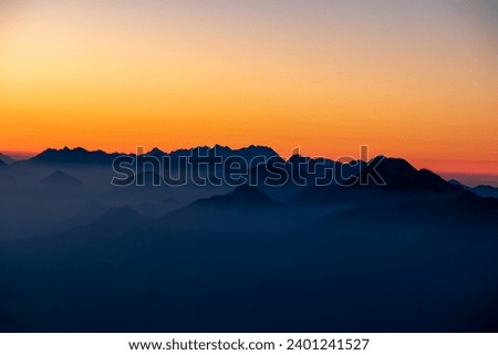 Panoramic sunrise view from Dobratsch on the Julian Alps and Karawanks in Austria, Europe. Silhouette of endless mountain ranges with orange and pink colors of sky. Jagged sharp peaks and valleys Royalty-Free Stock Photo #2401241527