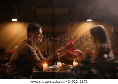 Happy young couple celebrating Valentines day having romantic dinner at home. Loving man giving gift box his woman. Copy space Royalty-Free Stock Photo #2401241873