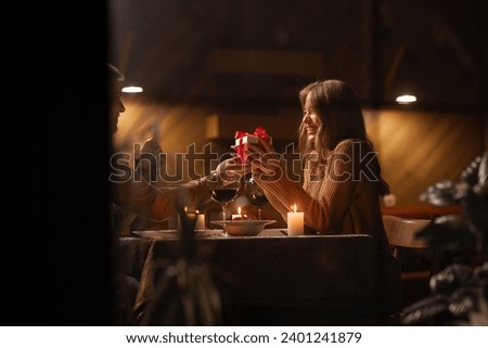 Valentine's Day concept. Happy couple in love celebrating Valentine's Day in the restaurant, trough window view. Man give gift to his wife. Copy space Royalty-Free Stock Photo #2401241879
