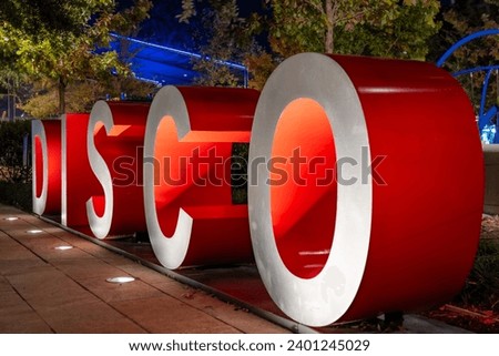 Red and gray three-dimensional 3d letters forming the word DISCO with an evening outdoor background.
