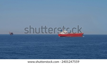 View of the stern of a merchant ship carrying crude oil is underway at sea in calm weather , an oil drilling unit is also visible in the background Royalty-Free Stock Photo #2401247559