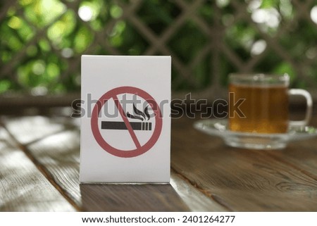 No Smoking sign and cup of drink on wooden table against blurred background, selective focus
