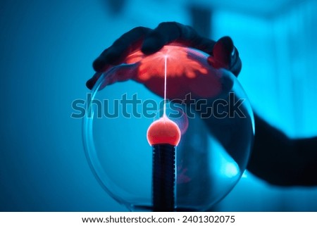 plasma ball. Hands holding plasma light ball. Plasma ball light ray science. Finger touching Plasma ball with smooth magenta blue flames. Electromagnetic Fields in a glass globe. Royalty-Free Stock Photo #2401302075