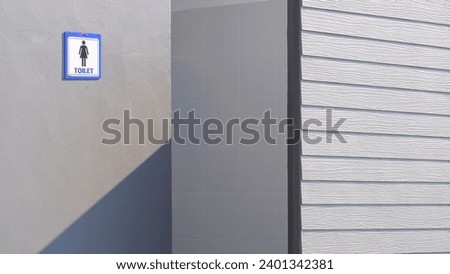 Perspective side view of artificial wooden blind fence in front of gray concrete wall of outdoor female restroom in public area