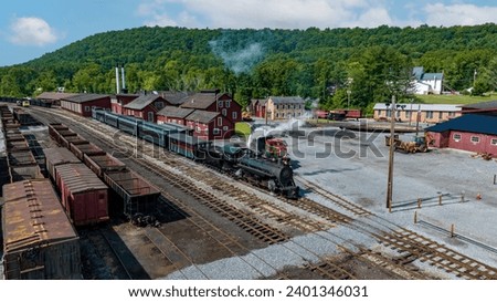 An Aerial View of a Narrow Gauge Steam passenger Train, Leaving the Yard for a Days Work, on a Sunny Summer Day Royalty-Free Stock Photo #2401346031