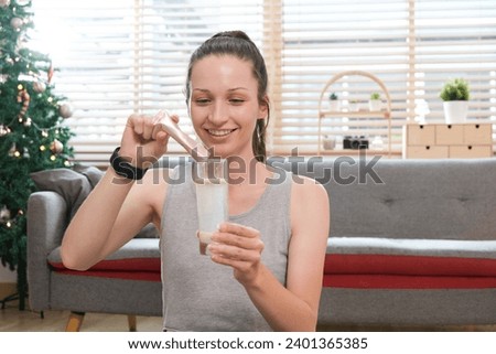 Young caucasian woman preparing healthy supplement after exercise dissolving collagen powder in glass of water..