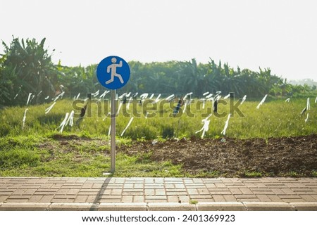 Jogging track with blue running sign in outdoor park with greenery open fields view in the morning.