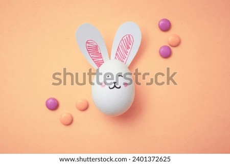 Chicken eggs with cute bunny faces and rabbit ears on pastel peach background. Sweet candy. Happy Easter. Food photo. White empty egg for coloring. Coloring book for children. Trendy beige color 2024