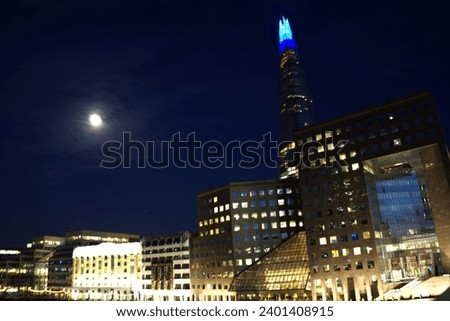 
London night: Skyscrapers touch the full moon, a celestial glow mirrored in city lights—a skyline ballet under the midnight sky