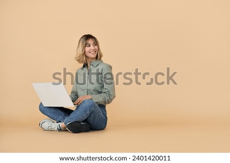 Happy pretty gen z blonde young woman with laptop, smiling european student girl with short blond hair using computer elearning online sitting isolated on beige background looking at copy space.